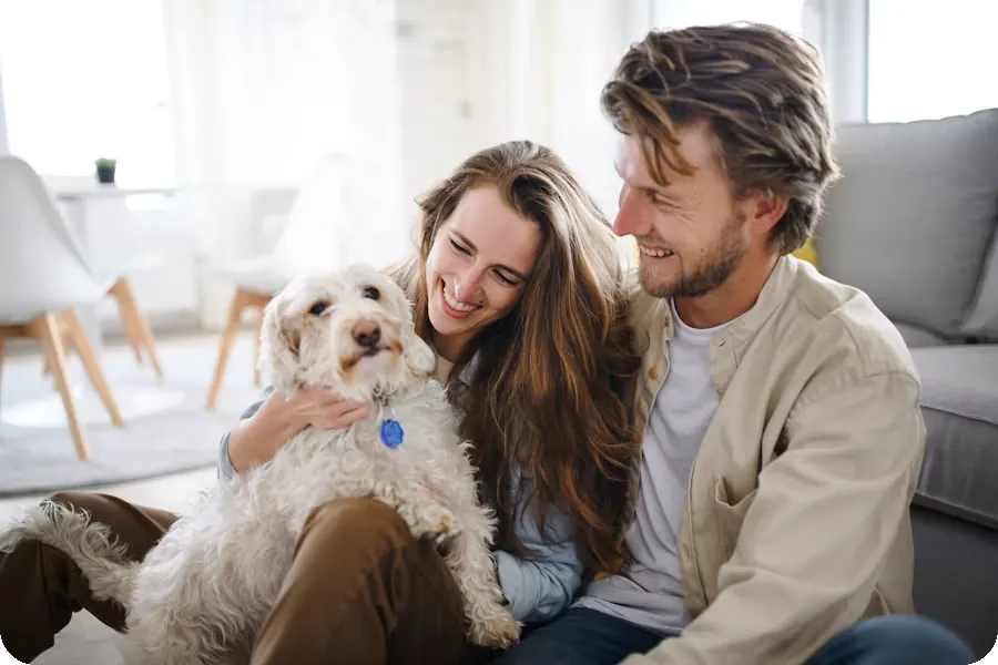 A happy couple sitting on the floor with their fluffy white dog in a bright, modern living room.